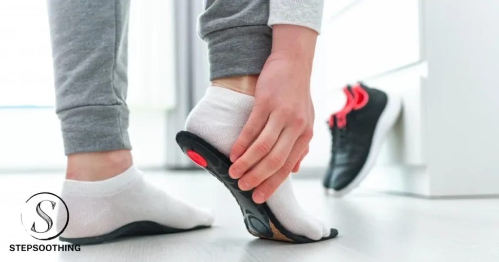 A person trying is checking the size of black insole, wearing white socks and grey trousers on white floor having white furniture.